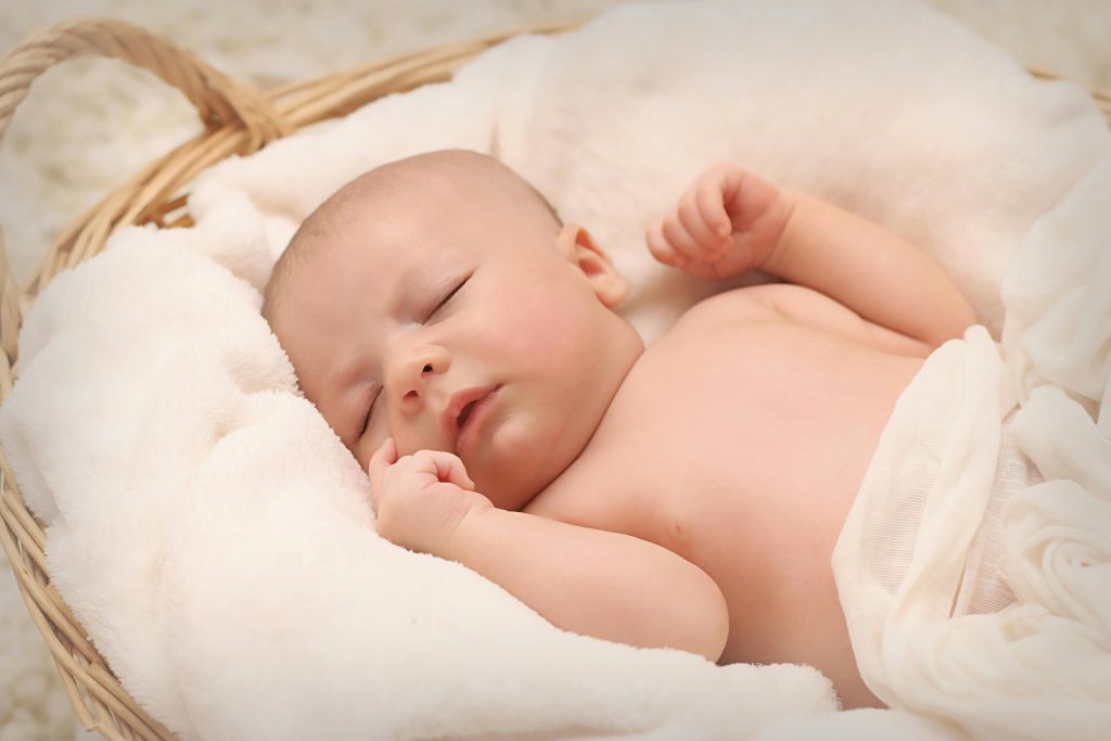 A peaceful sleeping baby nestled in a soft, fluffy blanket inside a wicker basket.