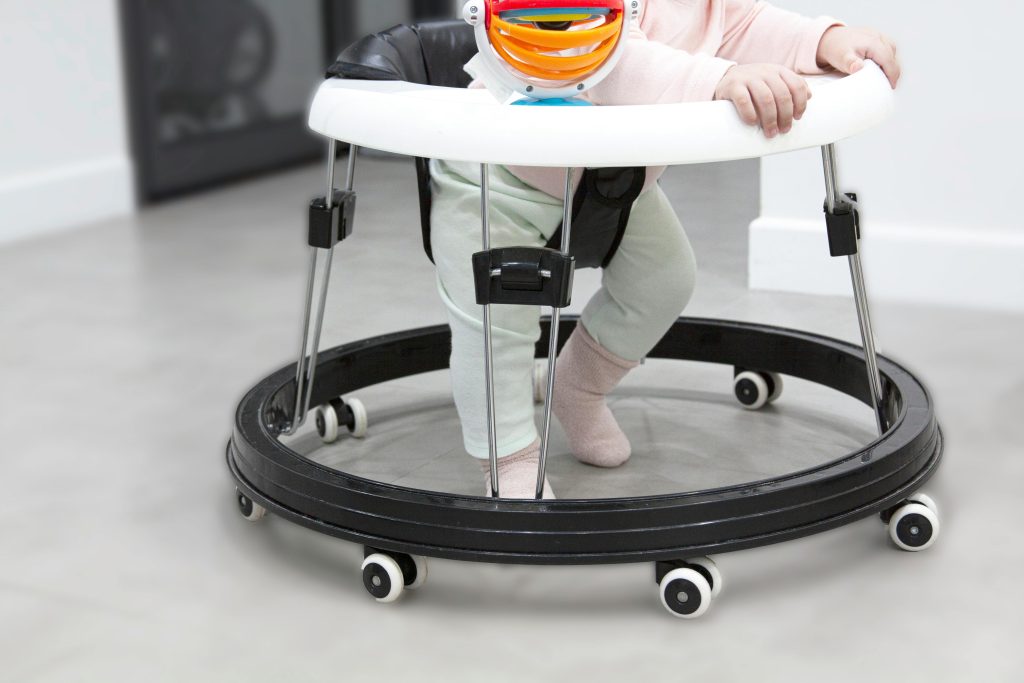 Adorable baby learning to walk using a colorful baby walker indoors.